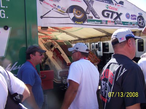 1972 Ford Ranchero - A drag racing car with a distinctive livery is parked under a tent, with spectators nearby.