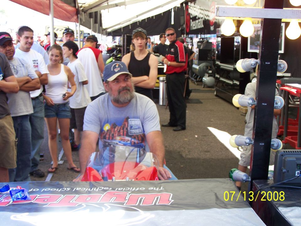 Man in blue cap and t-shirt with Ford Tough graphic sits behind a table with a red object