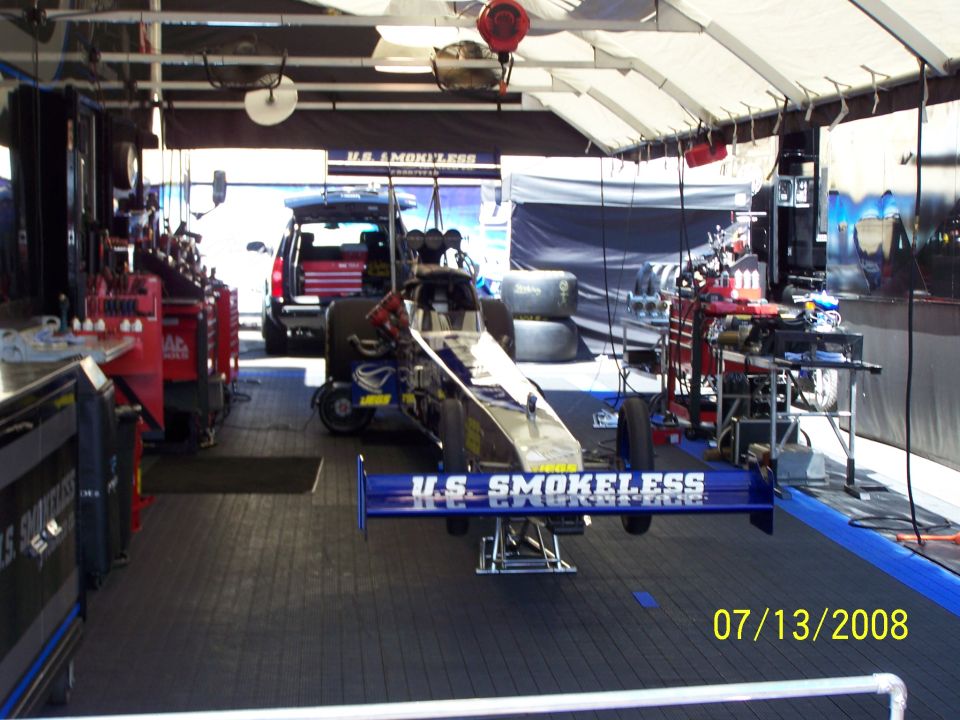 Dragster with 'U.S. SMOKELESS' on rear wing, parked in pit area with SUV and tools