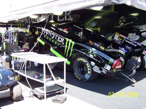 1972 Ford Ranchero - A black drag racing car with Monster Energy livery is parked in a garage, displaying various sponsor decals.