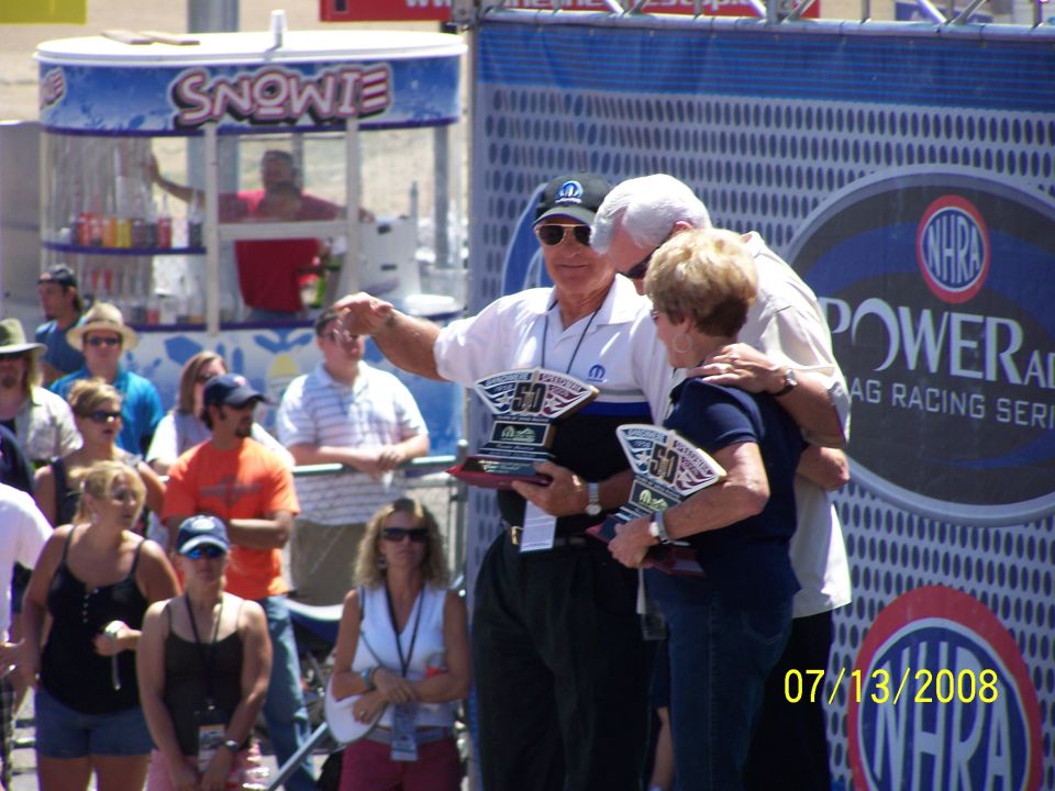 People on a stage holding trophies with '50' on them. A 'Snowie' stand is in the background