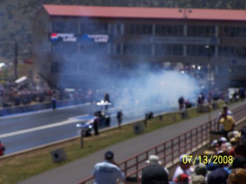 1972 Ford Ranchero - Drag racing event with smoke billowing from the track, spectators in the stands, and a building overhead.