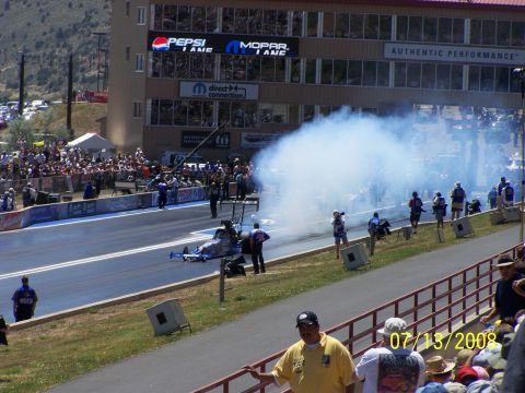 1972 Ford Ranchero - A dragster creates a large cloud of smoke on the track during a race event, with spectators watching from the stands.