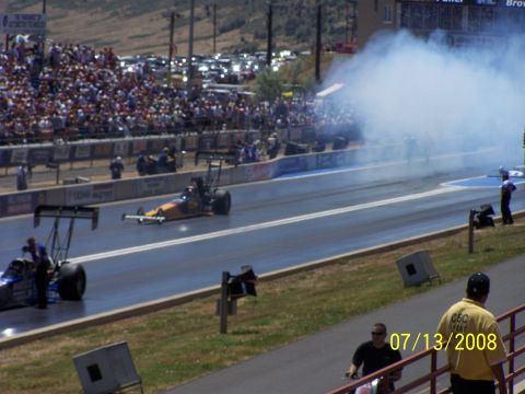 1972 Ford Ranchero - Two drag racing cars compete on a track, with a large crowd watching and smoke billowing from one of the vehicles.