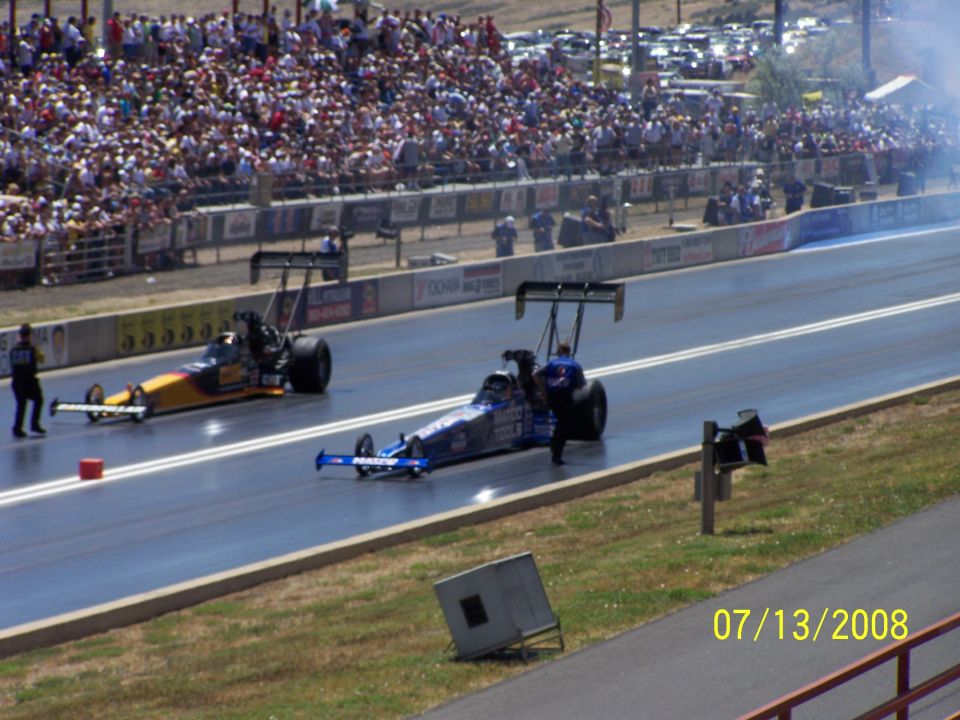 Two drag racing cars on a track with a large crowd in the stands