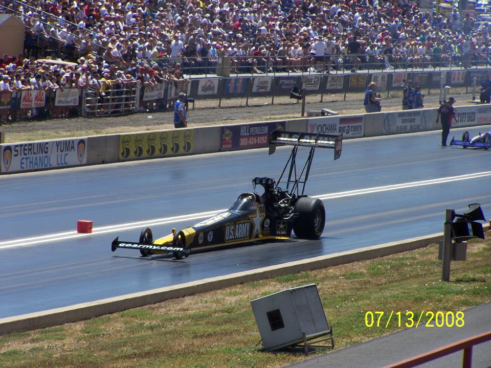 Dragster with U.S. Army livery on a drag strip, crowd in background. Another dragster visible in distance