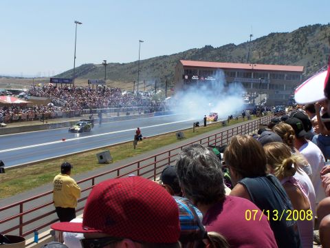 1972 Ford Ranchero - A drag race is underway with two cars on the track, surrounded by cheering spectators and billowing smoke.
