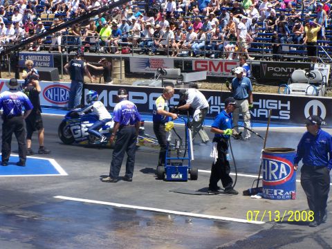 1972 Ford Ranchero - A drag racing motorcycle and crew prepare on the track, with a crowd watching from the stands.