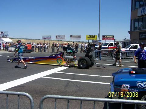 1972 Ford Ranchero - A dragster is positioned on a race track with spectators and buildings visible in the background.