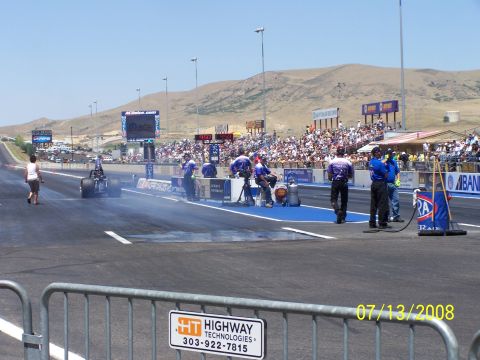 1972 Ford Ranchero - A dragster prepares for a run at Bandimere Speedway, with crowds filling the stands on a sunny day.