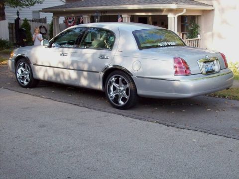 1998 Lincoln Town Car - A silver sedan with chrome wheels is parked in front of a house.