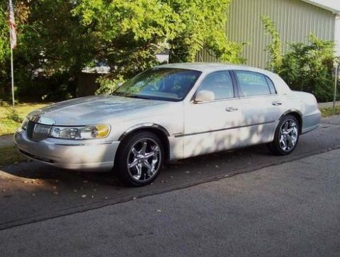 1998 Lincoln Town Car - A silver 1998 Lincoln Town Car is parked on the side of a street with trees and a building in the background.