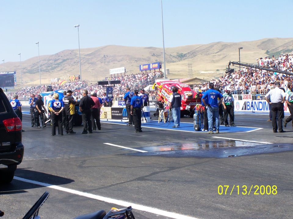 Drag racing scene with a red dragster and a blue dragster on the track, spectators in the stands, and a date stamp of 07/13/2008