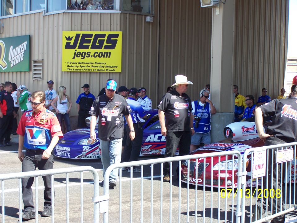 Drag racing cars and crew members in front of a building with JEGS signage