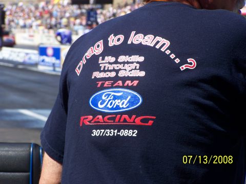 1972 Ford Ranchero - A spectator at a drag racing event wears a Ford Racing t-shirt with a phone number and slogan.