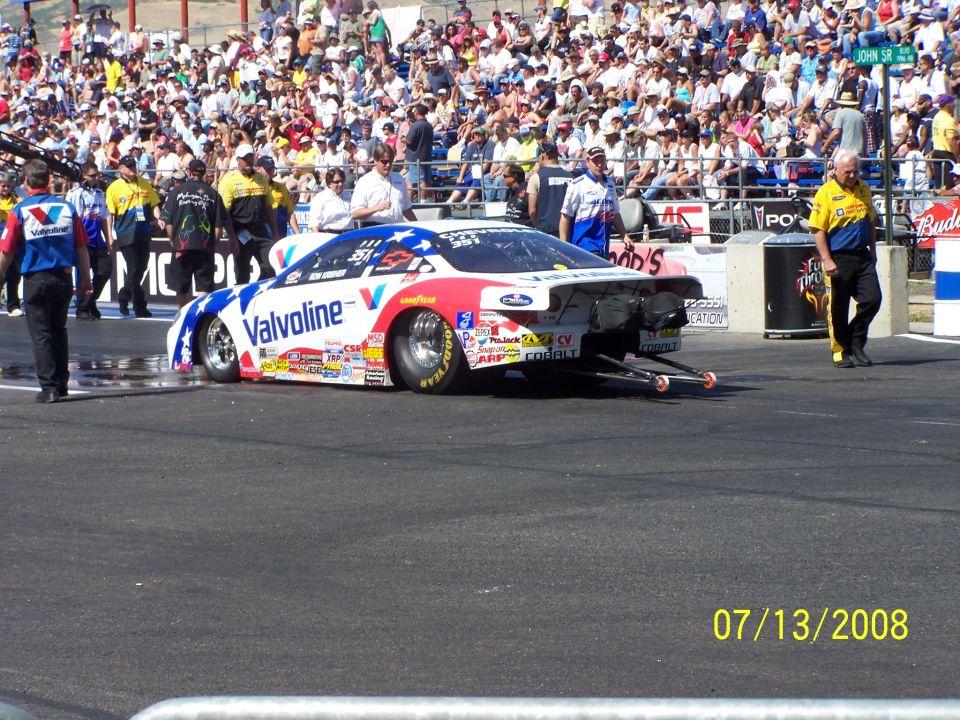 Drag racing car with Valvoline livery on track, crowd in background