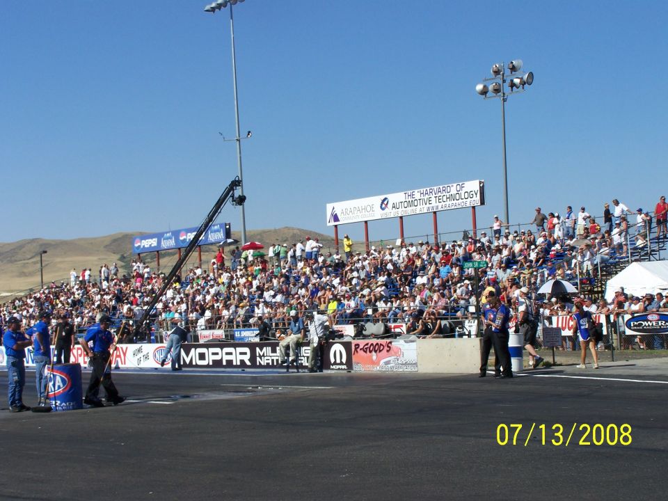 Drag strip with packed grandstands, a camera crane, and sponsor banners under a clear blue sky. Date stamp reads 07/13/2008