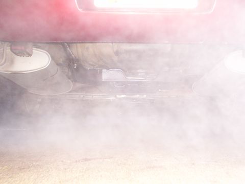 1998 Ford Taurus - Smoke billows from the rear of a red vehicle, obscuring the undercarriage and exhaust pipe.
