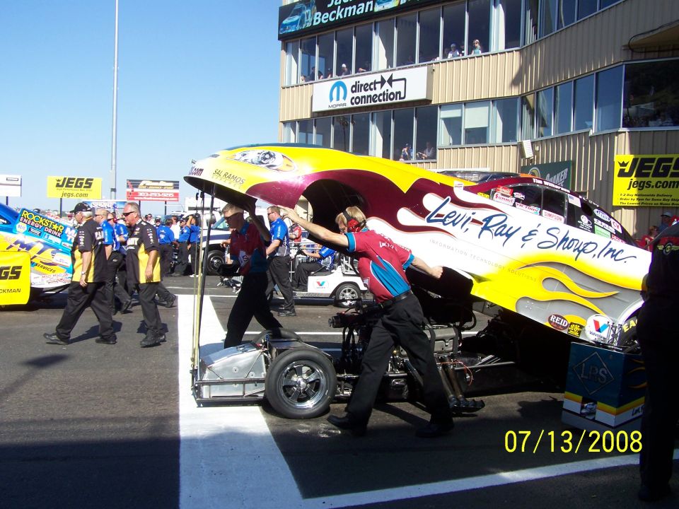 Yellow and red drag racing car body with flames, being serviced by crew