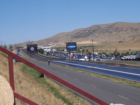 1972 Ford Ranchero - A drag strip scene with scoreboards and numerous vehicles parked in the distance under a clear sky.