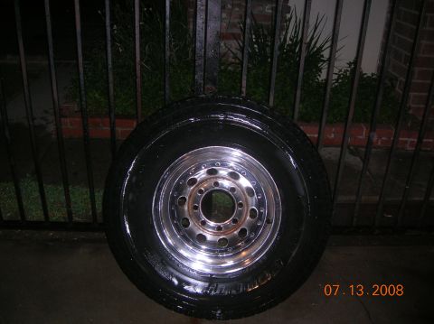 1985 Ford Bronco - A single tire and wheel assembly is shown, wet, in front of a fence and brick wall.