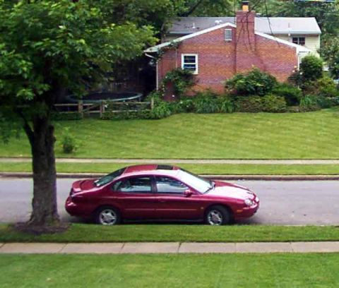 1998 Ford Taurus - A red 1998 Ford Taurus is parked on the side of the road in a suburban neighborhood.