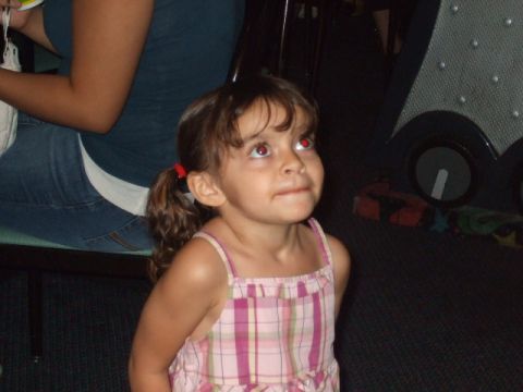 2008 Jeep Cherokee - A young girl with red-tinted eyes looks upwards while wearing a pink plaid dress.