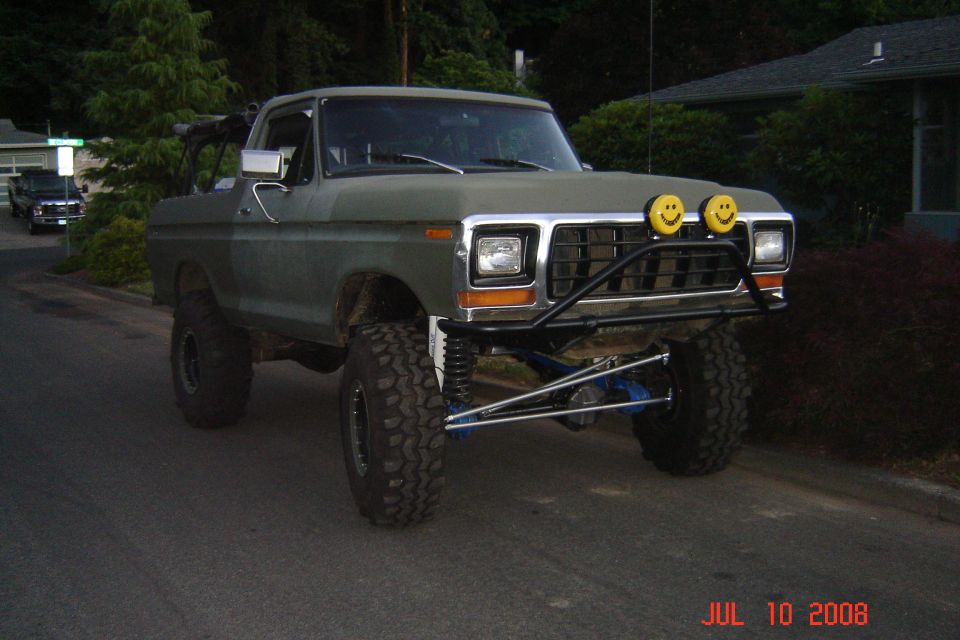 Olive green 1978 Ford Bronco with lifted suspension, off-road tires, and smiley face headlights