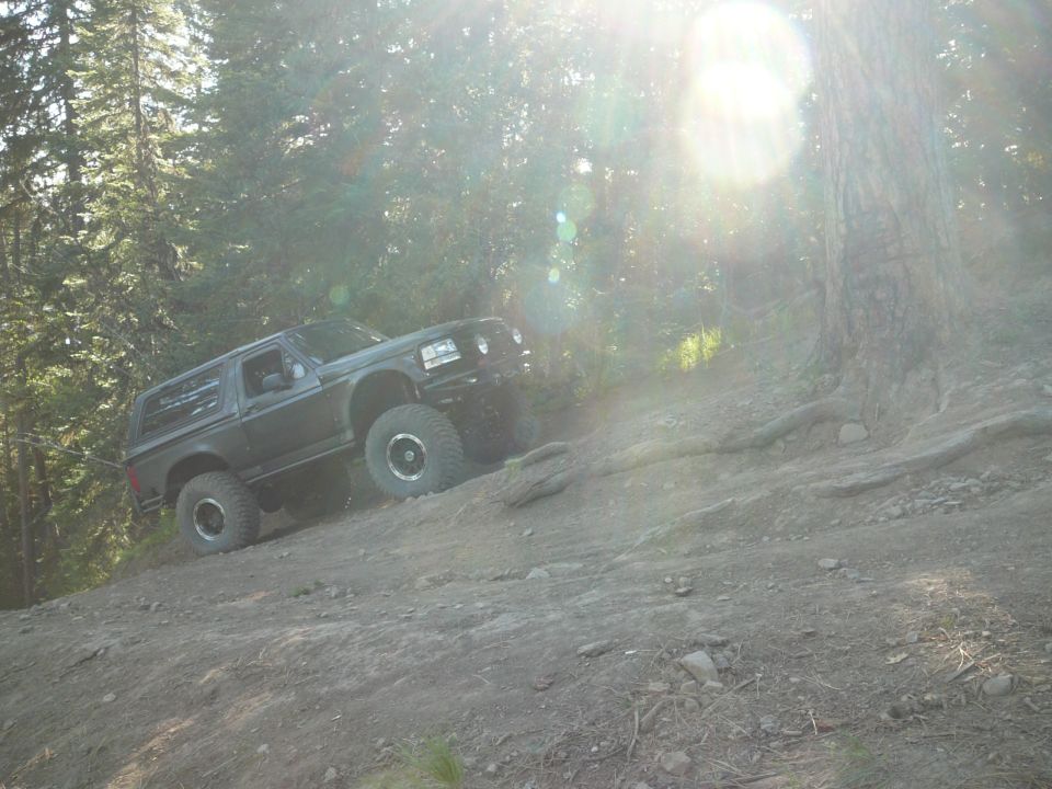 Black Ford Bronco climbing a dirt hill in a forest