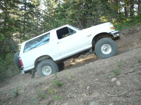 1991 Ford Bronco - This Ford Bronco is navigating a challenging off-road trail, kicking up dirt as it ascends the slope.