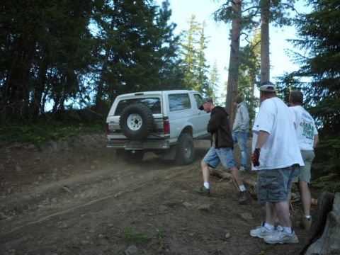 1991 Ford Bronco - A white Ford Bronco navigates a dirt trail as several people watch.