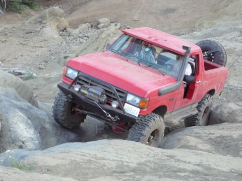 1991 Ford Bronco - This modified SUV navigates a challenging rocky course, its snorkel and winch indicating off-road capability.