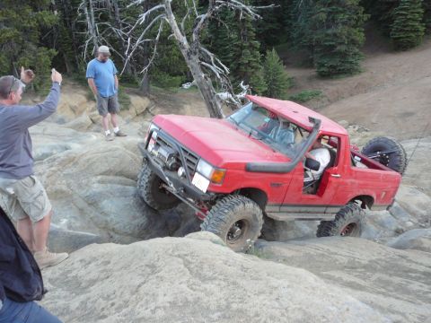 1991 Ford Bronco - Red off-road SUV navigates a rocky incline, its off-road capabilities.
