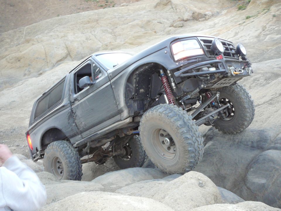 Dark grey SUV with lifted suspension and large tires climbing over rocks