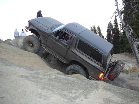 1991 Ford Bronco - A dark gray Ford Bronco navigates a steep, rocky terrain during an off-road excursion.