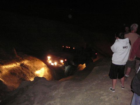 1991 Ford Bronco - A 1991 Ford Bronco navigates a dark, off-road trail at night, its headlights illuminating the terrain.