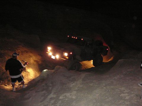 1991 Ford Bronco - Off-road vehicle navigates a challenging dirt path at night, illuminated by its own lights and a nearby flashlight.