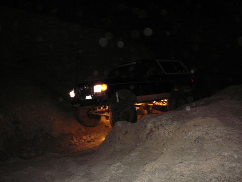 1991 Ford Bronco - A Ford Bronco navigates a rocky trail in the dark, illuminated by its headlights and undercarriage lights.