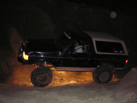 1991 Ford Bronco - A modified Ford Bronco navigates an off-road trail in the dark, illuminated by its headlights and underglow.