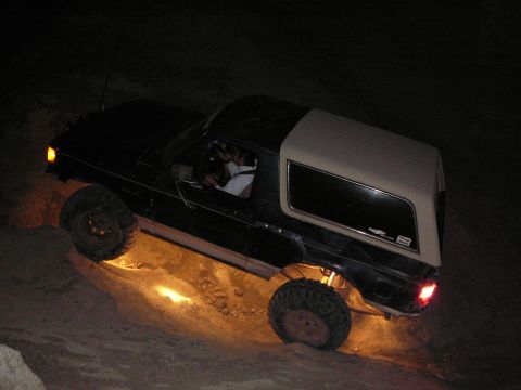 1991 Ford Bronco - A Ford Bronco navigates a challenging dirt incline in the dark, with its undercarriage lights casting an orange glow.
