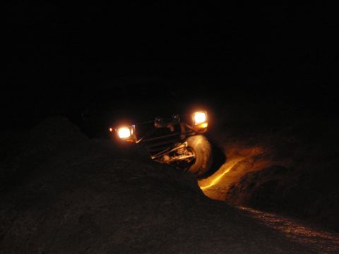1991 Ford Bronco - An off-road vehicle drives through a dark, uneven landscape, its headlights illuminating the path.