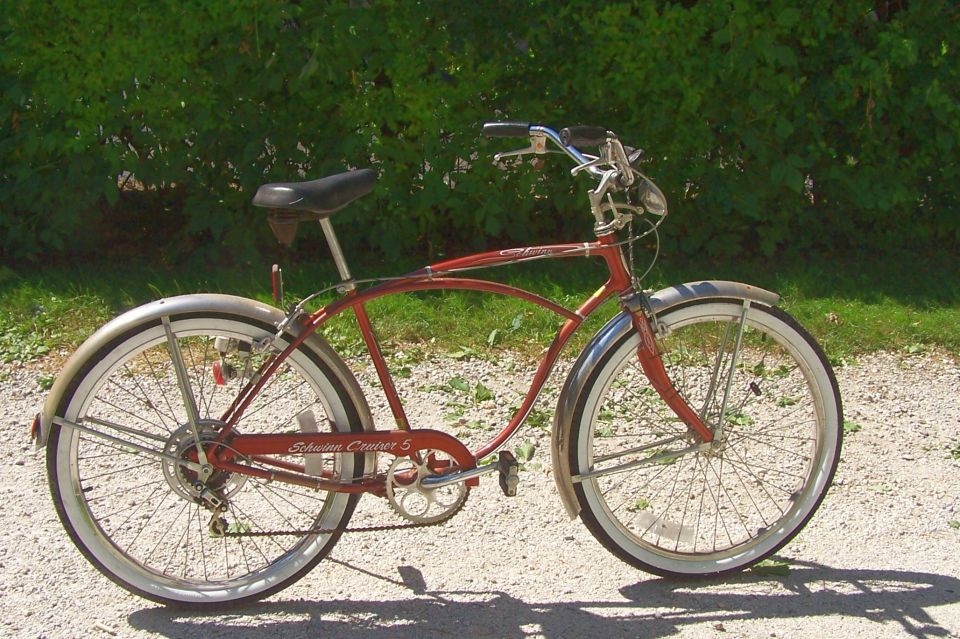 Red Schwinn Cruiser bicycle parked on gravel near greenery