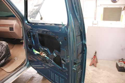 1996 Ford Bronco - Interior view of a teal SUV door, showing exposed mechanisms and a beige dashboard, possibly undergoing repair.
