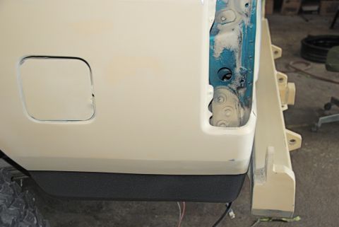1996 Ford Bronco - The rear quarter panel of a vehicle is shown with primer applied, revealing exposed metal and part of a tow hitch assembly.