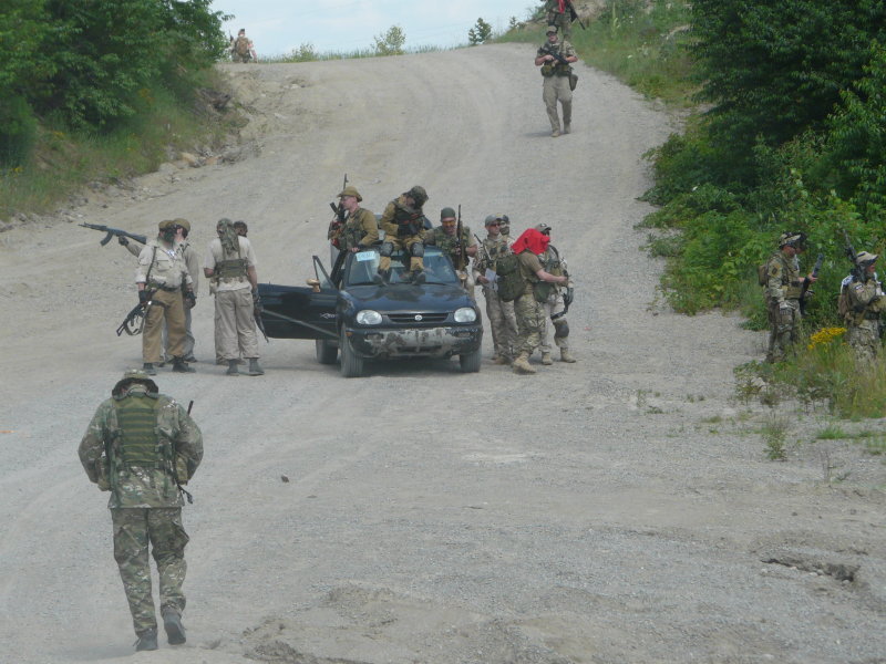 Black hatchback with people on and around it on a dirt road