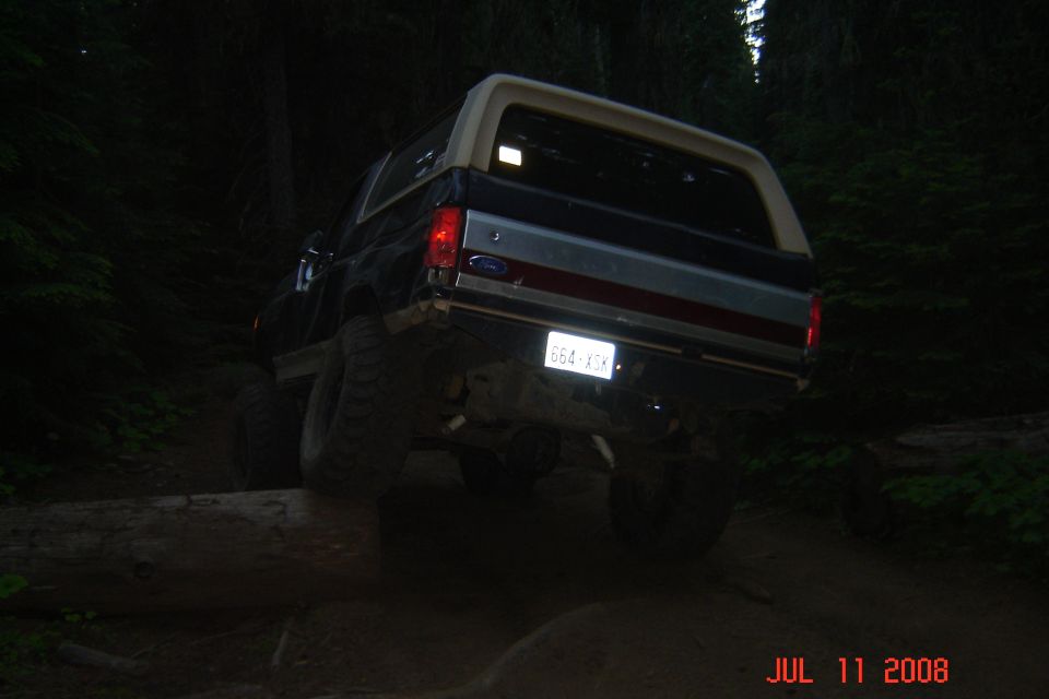 Lifted Ford full-size SUV climbing over logs in dark forest