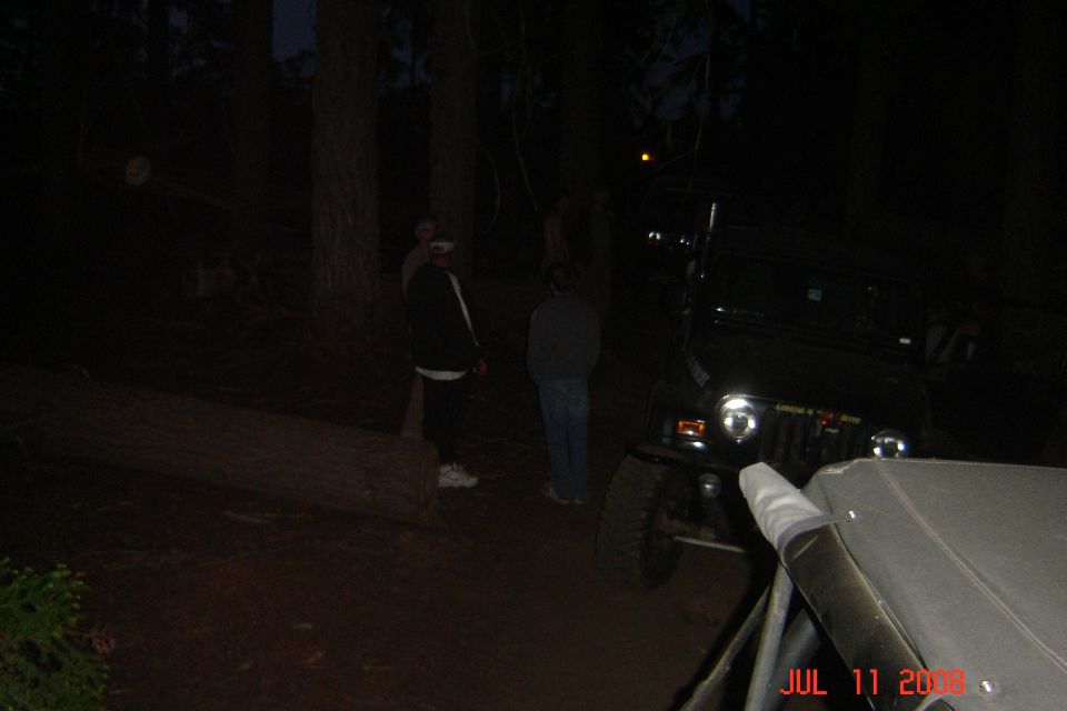 Black Jeep Wrangler parked at night with people standing nearby. Another vehicle's interior is in the foreground