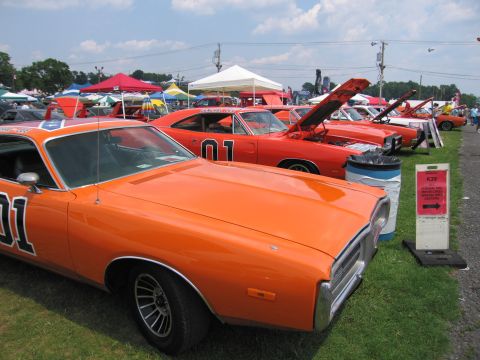 2001 Ford Crown Victoria - Multiple General Lee replicas are displayed at a car show under a partly cloudy sky.