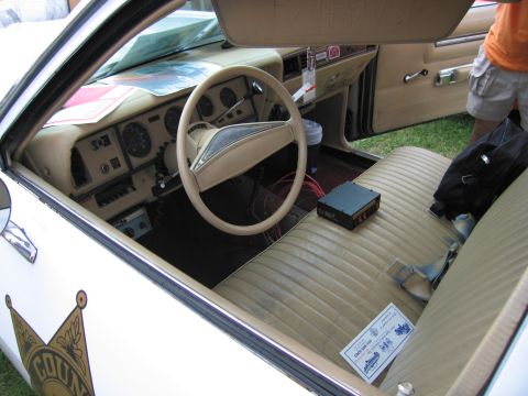 2001 Ford Crown Victoria - The interior of a vintage police car shows a tan bench seat and dashboard with visible wiring and equipment.