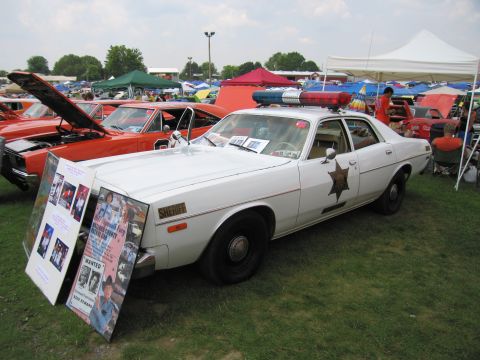 2001 Ford Crown Victoria - A vintage sheriff's car is displayed at an outdoor event, with informational posters placed in front of it.